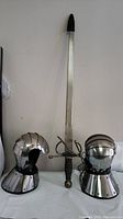 Full view of Toledo Salamanca sword standing upright between two metal gauntlet gloves with segmented armor plating and black interior lining.
