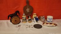 Full view of the collectibles arranged with a horse figurine, Cuss Box, ceramic steins, miniature house, mug, Paragon dish, and glass and metal items.