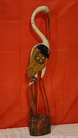 Full view of the wood carved blue heron standing against a red backdrop, showing its full height and base.