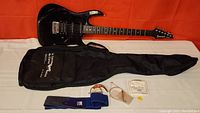 All lot items laid out: guitar, gig bag, capo, strap, strings pack, and pick