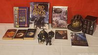 Full lot with all Tolkien books, boxed Oracle card set, snowglobe figurines, CD, and figures on red background