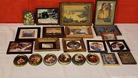 Full lot overview of all framed prints and decorative plates arranged on white surface against red background.