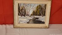 Full view of framed oil painting depicting a spring brook flowing through a snow-covered forest with birch and pine trees.