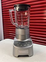 Photo of Cuisinart blender showing the metallic base, glass pitcher with handle, black lid, and front control panel with function buttons.