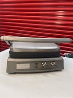 Side view of the closed Cuisinart panini press showing the front control panel with two knobs and indicator lights, and the silver body.