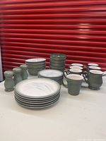 Full set arranged showing all types of items in the lot including bowls, plates, mugs, and salt and pepper shakers in blue/green colors.
