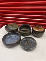 Front view of five rustic pottery bowls of varying sizes and colors, arranged on a white surface with a red background.