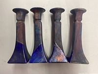 Four tall Raku ceramic candlesticks arranged side by side showing shape and glaze detail with iridescent blue and purple tones.