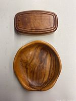 Top-down view of a rectangular wooden box with lid above it and large wooden salad bowl below. Both items have rich natural wood grain patterns.