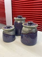 Front and side view of three blue and green glazed pottery canisters with lids by Barb Howe, showing different heights and colors.