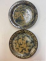 Top view of two decorative pottery plates showing their leaf and vine patterns with glazed rims.
