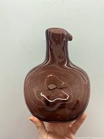 Deep mauve glass vase shown from front, highlighting rounded body and small top spout held by hand.