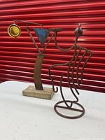 Photo showing two metal art pieces: a kinetic art sculpture with a yellow disc and blue triangle on a metal base, and another abstract curved rib-like metal sculpture.