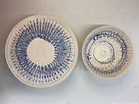 Top view of white pottery cake plate with blue radial pattern and matching bowl with similar pattern inside and on rim, displayed side by side