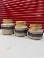 Front view of the three pottery canisters, showing beige and blue horizontal stripe design and cork tops.