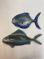 Top and front view of two pottery fish wall hangings in blue and green tones, showing detailed textures and colors.