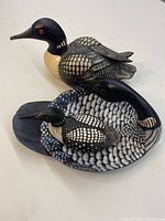Top and side view of two wooden loon figurines resting together on a white surface.