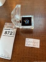 10K gold ring with a blue synthetic spinel gemstone displayed in a clear square box with a black velvet interior.