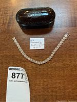 Bracelet laid flat on wood surface alongside black display case and handwritten note detailing carat weight and quality