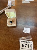 Ring and handwritten seller note reading “10K Onyx 1250” alongside MaxSold lot tag in open velvet box on wood surface.