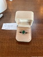 Ring in presentation box with handwritten note indicating 14K assembled green triplet and diamond .18 replacement value $1025