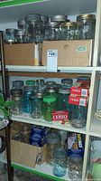 Top and second shelf showing clear and colored glass mason jars in and out of cardboard boxes