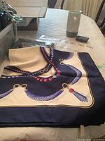 Folded scarf on table showing navy and ivory pattern with chain and bead motif