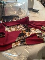 Scarf displayed fully laid out on table showing red border and chain print pattern.