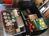 Two large plastic bins filled with assorted Christmas balls and boxed decorations including metallic silver balls, star and angel shapes, and reindeer figurines.