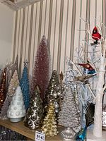 Photo showing a collection of Christmas trees of varying sizes and colors such as white, gold, blue, and pinkish-purple with bubble and textured designs.
