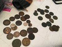 Wide view of assorted vintage coins scattered on a white surface with a brown drawstring pouch in background.