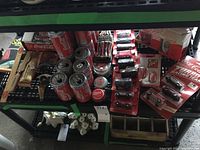 Photo showing multiple Coca-Cola unopened cans, some bottle openers in packaging, various miniature boxed Coca-Cola cars, next to some wooden item organizers