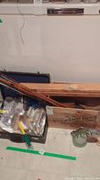 Overview of wooden crate containing collapsed fishing rods, plastic tackle box with feathers, and ceramic fish figurine
