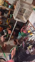 Overview of basement area showing various gardening items including flamingo yard figures, white bird cage on stand, many planters, and a basket of garden stakes with faux plants.