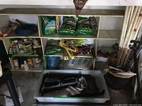 Full view of storage shelving with various gardening supplies including tools, bags of fertilizer and seed, garden hose, and ceramic plant pot.