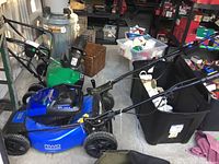 Side view of blue Kobalt mower with handle assembly and green mower visible in background