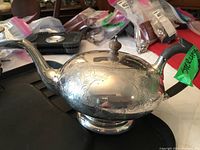 Front view of domed sterling teapot on quilted surface with background items