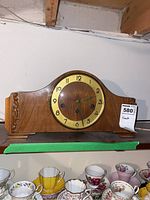 Full view of wooden mantel clock showing its curved top and clock face with Arabic numerals.