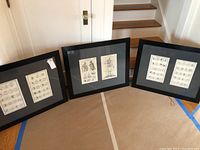 Three black frames arranged on the floor, each with two antique European prints inside.