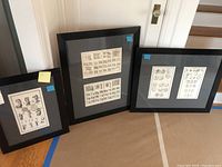 Three framed antique prints arranged on floor against wall showing different sketches and coat of arms.