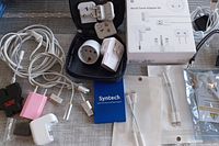 Overview of assorted electronic adapters and cords including Syntech USB charger, Apple World Travel Adapter Kit box, cables, and plug adapters.