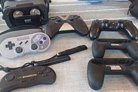 Photo showing the VR Shinecon headset, 8BitDo and Playstation controllers, SNES-style gamepad, and Nintendo Switch grip holders arranged on a surface