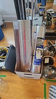 Photo showing two rolls of double reflective insulation sheeting in a cardboard box alongside other items on the floor.