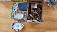 Overview image showing a box with various kitchen utensils and tools, ceramic plates, metal serving tray, and a blue textured ceramic piece.