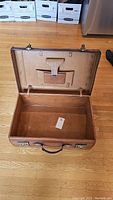 Opened antique leather suitcase showing interior lining and small pocket.