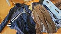 Nike black track jacket, brown button down shirt, and other assorted shirts and outerwear laid out on floor