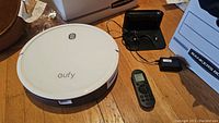 White circular Eufy Robovac with one power button and brand name on top, sitting on wooden floor.