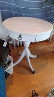 Full view of the round white painted antique side table with single drawer and tripod base.
