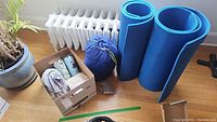 Photo showing two rolled blue foam mats, blue sleeping bag in sack, and box with clothes pins and tumblers