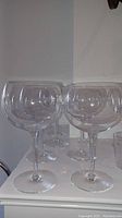 Nine clear wine glasses with large rounded bowls on a white surface.